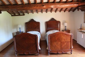 A room with two wooden beds, a nightstand with a lamp, a radiator, and a wooden ceiling. - "Torre di Sant'Ansano" Farmhouse (Siena)