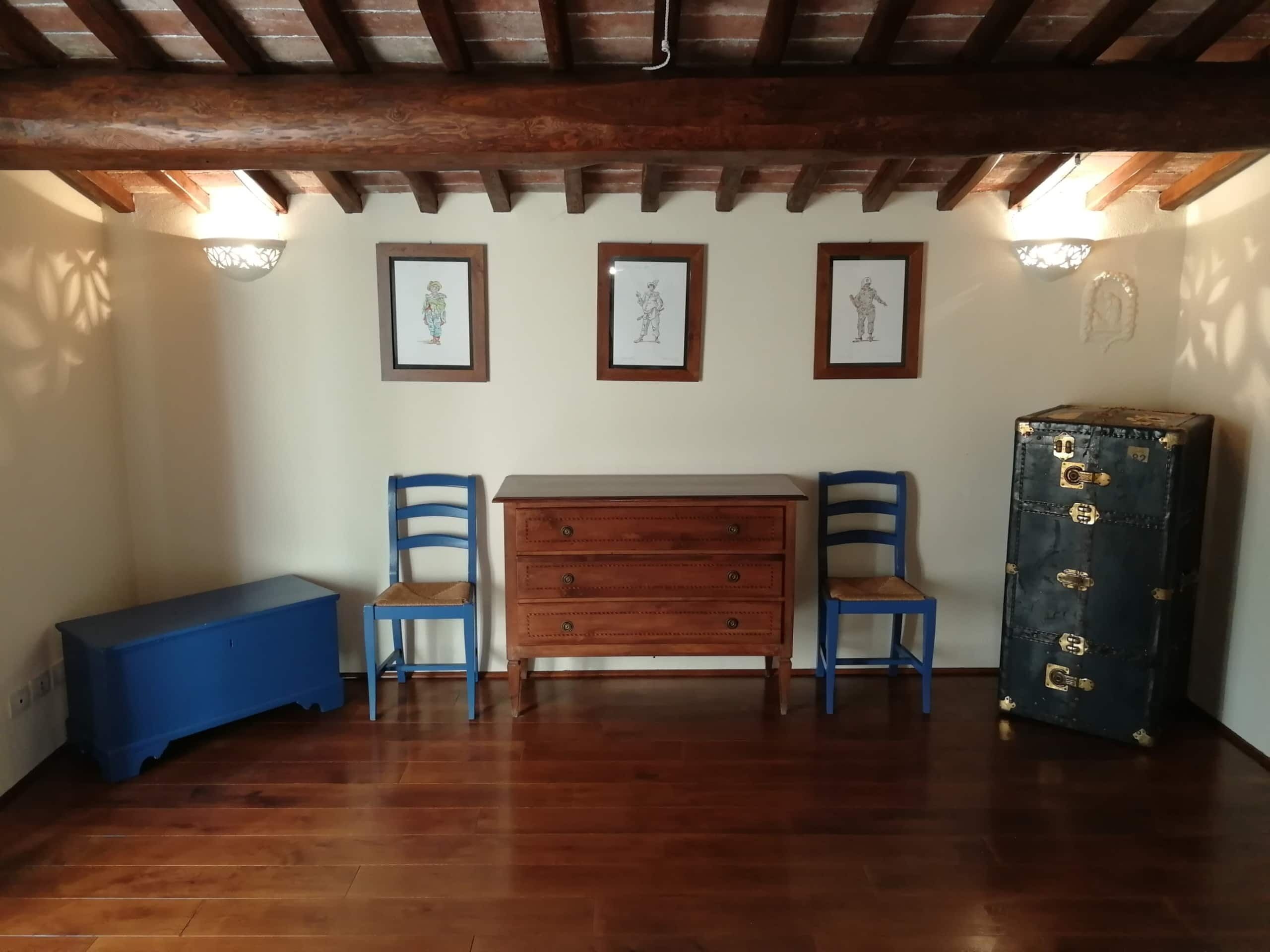 A room with wooden flooring, a wooden dresser, two blue chairs, and a vintage suitcase.