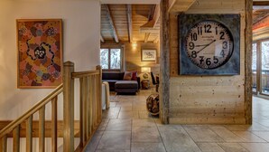A wooden interior with a large clock, a staircase, and a sofa in the background.
