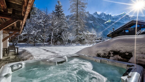A hot tub in a snowy outdoor setting with mountains in the background.