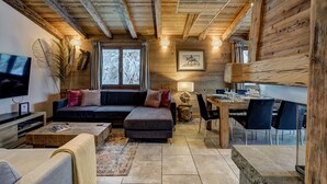 A cozy cabin interior with a wooden ceiling, a sofa, a dining table, and a TV.