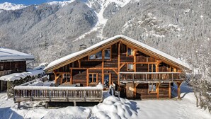 Um chalé de madeira com telhado inclinado, rodeado por montanhas cobertas de neve.