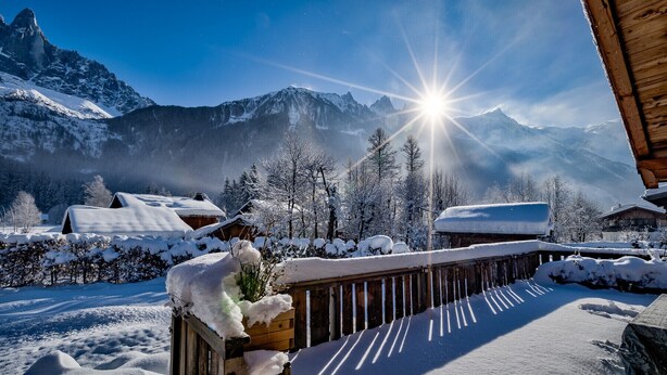 Paisagem montanhosa coberta de neve com uma cabana de madeira e um alpendre de madeira.