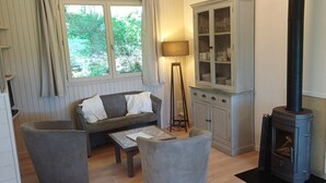 En hyggelig stue med sofa, lænestole, lampe, skab og en brændeovn.