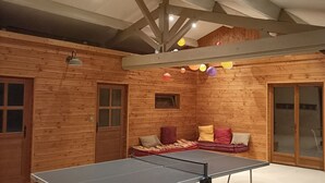 Et trægulvsrum med et bordtennisbord, en sofa med puder og et vindue.