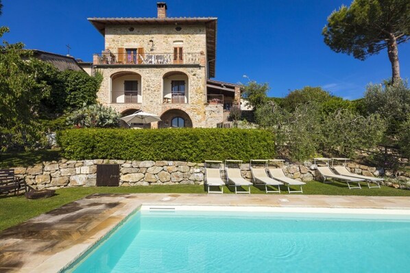 Una villa de piedra con piscina, sillones de descanso y un muro de piedra.