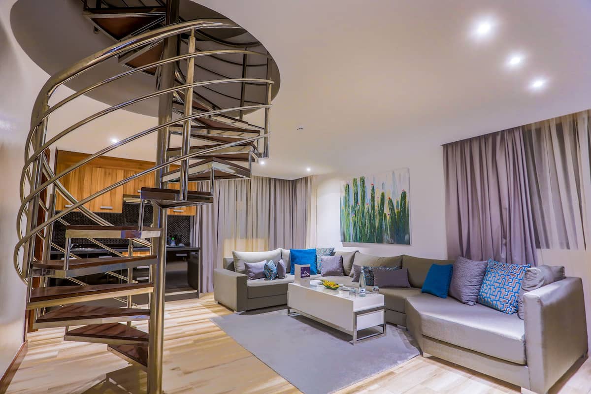 A modern living room with a spiral staircase, a sofa set, and a painting on the wall.