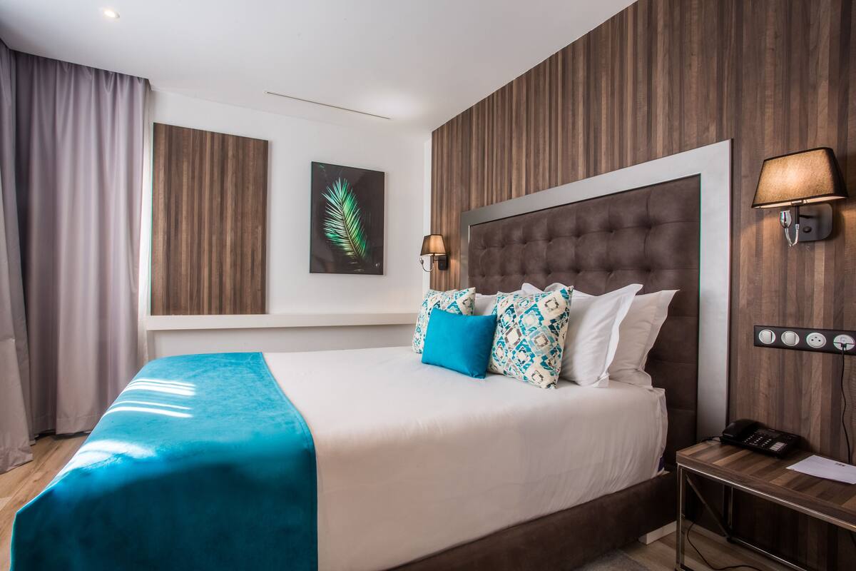 A hotel room with a large bed, a wooden headboard, a nightstand with a phone, and a wall-mounted lamp.