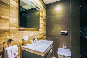 Un baño moderno con tocador de madera, un espejo grande, un lavamanos blanco y un inodoro.