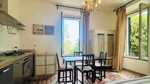 A compact room with a kitchenette, a dining area with chairs, a bed, and a window with curtains.
