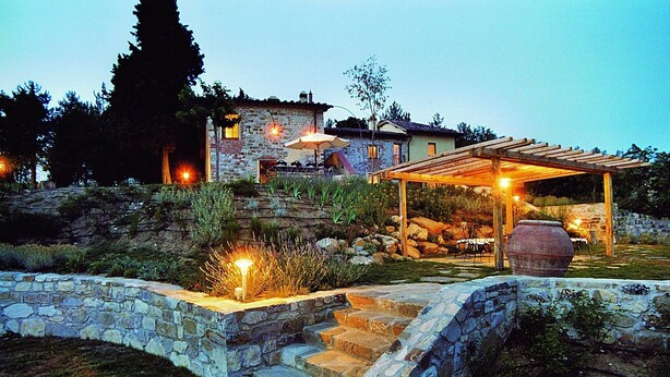 Una escalera de piedra conduce a una casa de piedra con una pérgola de madera y un área de estar al aire libre.