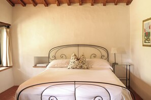 Une chambre à coucher avec un lit, une table de chevet, une lampe et une fenêtre avec des rideaux.