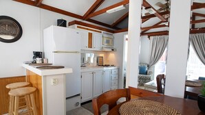 Uma cozinha compacta com geladeira, micro-ondas e fogão, banquetas de madeira e uma mesa de jantar com um jogo americano trançado.