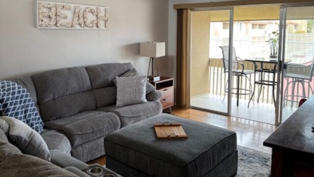 Una sala de estar moderna con un sofá seccional gris, un pequeño otomaní y una mesa de centro. Hay un letrero en la pared que dice "BEACH".