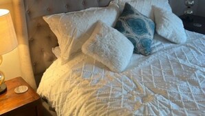 Un dormitorio con un cabecero capitonado, una colcha blanca acolchada y varias almohadas.