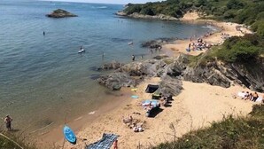 Ein Küstenstrand mit klarem Wasser, felsigen Ufern und Menschen, die unterschiedliche Aktivitäten ausüben.