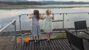 Zwei Personen auf einem Balkon mit Blick auf einen See und Berge in der Ferne.