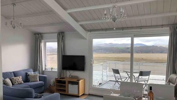 Ein Wohnzimmer mit einer Couch, einem Fernseher und einem Balkon mit Tisch und Stühlen.