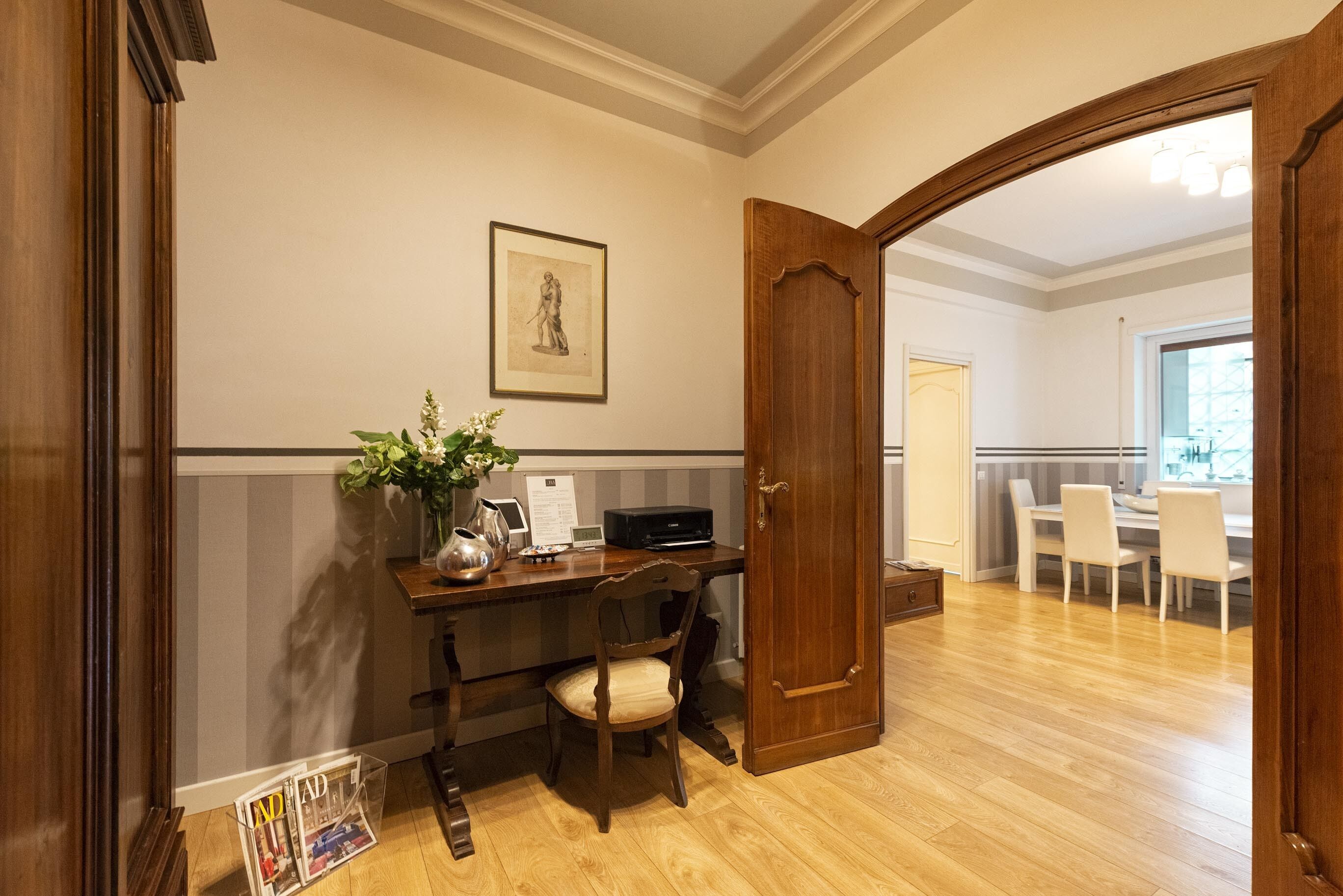 A wooden desk with a vase of flowers, a chair, and a framed picture on the wall.