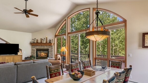 A cozy living room with a fireplace, a dining area with a large window, and a ceiling fan. - Short Walk to the Gondola Base (Steamboat Springs)