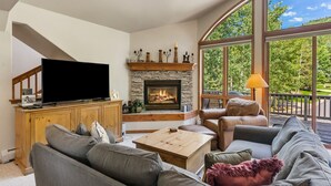 A living room with a fireplace, a television, and a large window with a view of greenery. - Short Walk to the Gondola Base (Steamboat Springs)