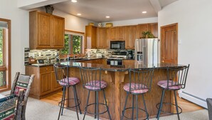 A modern kitchen with wooden cabinets, a stainless steel refrigerator, and a bar area with stools. - Short Walk to the Gondola Base (Steamboat Springs)