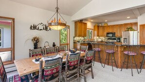 A dining area with a wooden table and chairs, a chandelier, and a view of the kitchen with wooden cabinets and a refrigerator. - Short Walk to the Gondola Base (Steamboat Springs)