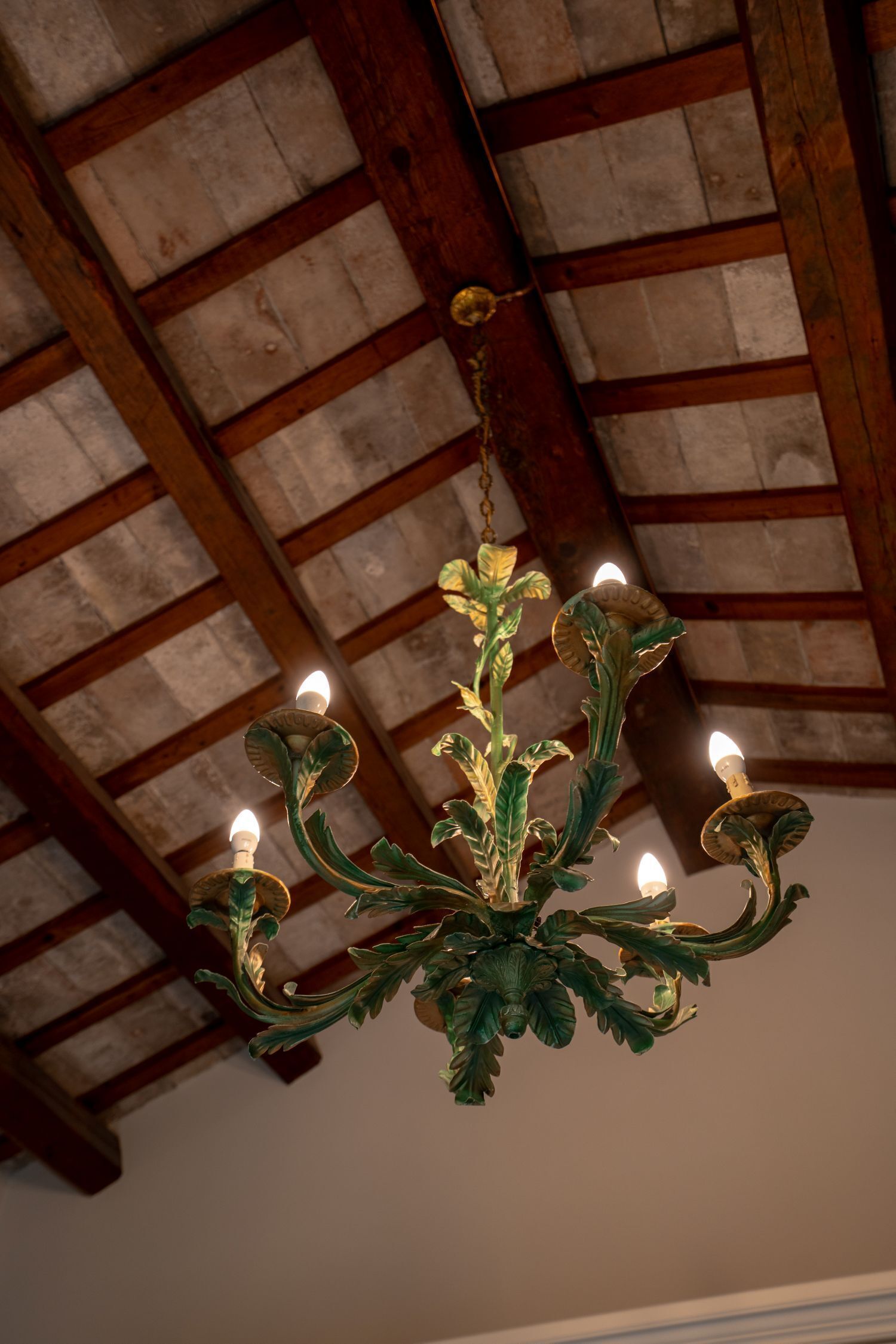 A chandelier with multiple candle-like lights, wooden beams, and a textured ceiling.
