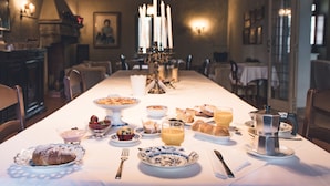 A dining table set with various breakfast items, including pastries, fruit, and beverages, in a warmly lit room with a chandelier and framed artwork on the walls.