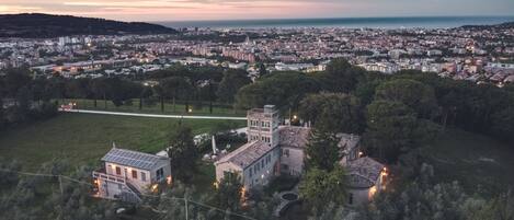 En vidsträckt utsikt över en stadssiluett i skymningen, med en framträdande historisk byggnad omgiven av grönska.