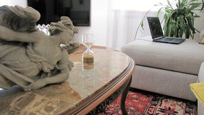 Una sala de estar con una mesa de centro de mármol, una estatua, una esfera de arena de vidrio, una computadora portátil, una planta y un sofá.