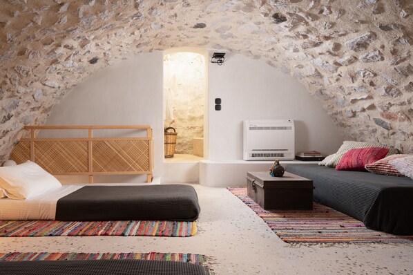 Une chambre confortable aux murs de pierre, avec un lit, une tête de lit en bois, une petite table et un banc.