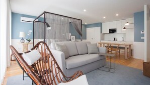 A modern living room with a grey sofa, wicker chairs, a dining table, and a kitchen area with white cabinets. - Downtown Luxury Studio w/ Balcony by Liiiving (Porto)
