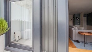 A modern interior with a sliding glass door leading to a living area, a sofa, a small table, and a potted plant. - Downtown Luxury Studio w/ Balcony by Liiiving (Porto)