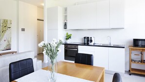 Une cuisine moderne avec des meubles blancs, une table à manger en bois et un vase rempli de fleurs.
