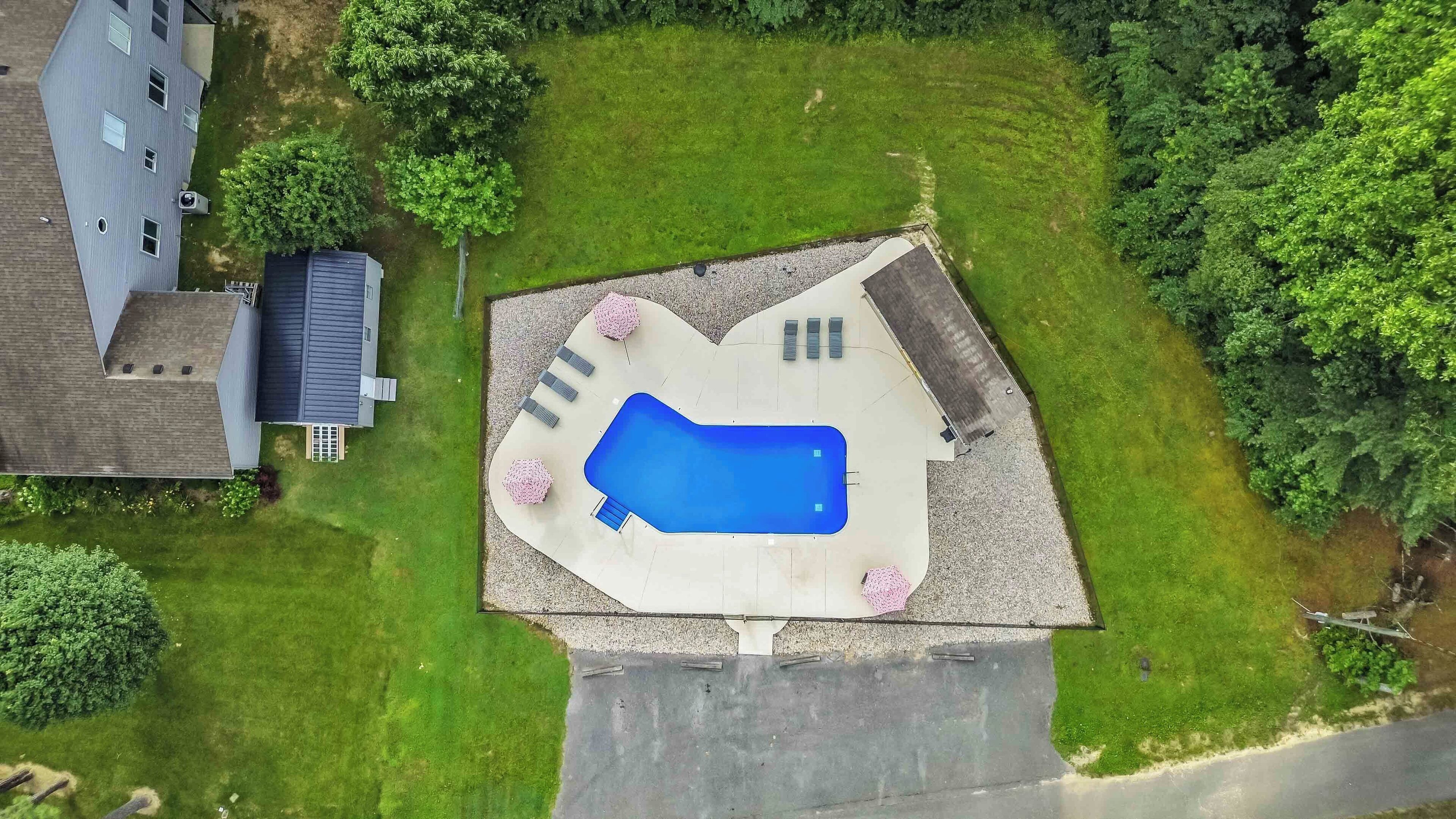 An aerial view of a residential property with a swimming pool, a covered patio, and a lawn.
