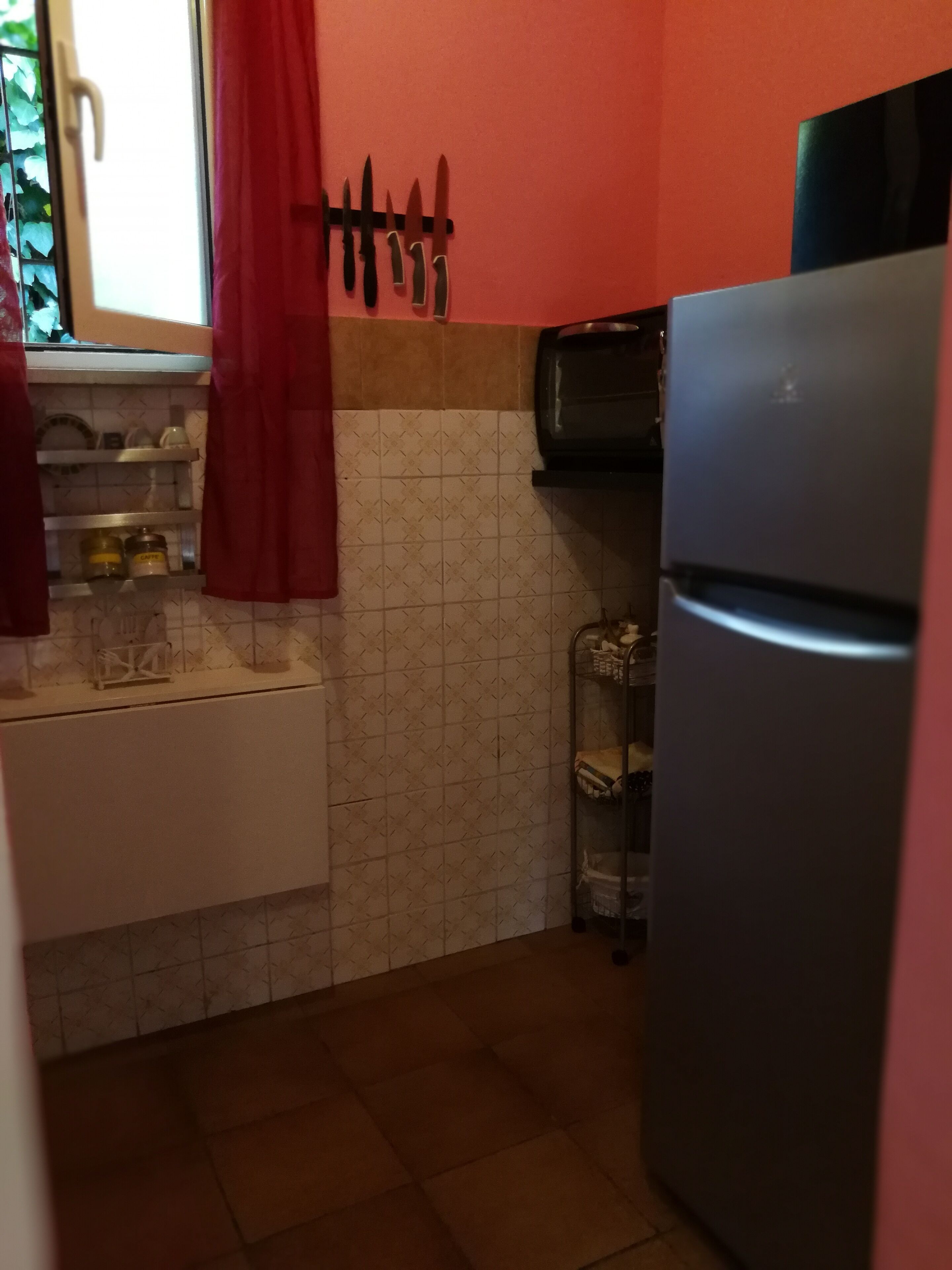 Una cocina con refrigerador, lavamanos y ventana con cortinas.