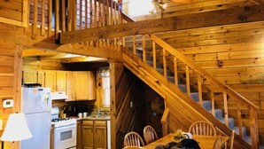 A wooden cabin interior with a kitchen, dining area, and a spiral staircase. - Wild and Wonderful Wilderness Cabin! (Hico)