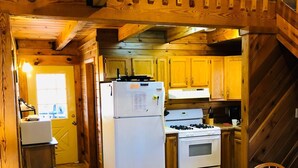 A wooden interior with a kitchen area featuring a refrigerator, stove, and wooden cabinets. - Wild and Wonderful Wilderness Cabin! (Hico)