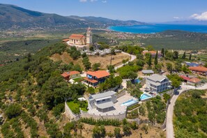 An aerial view of a coastal village with a prominent church, several residential buildings, and a clear view of the sea. - Demargia Villa A - Apartment in quiet area with communal pool suitable for 6 (Zakynthos)