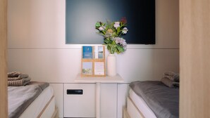 A bedroom with two beds, a flat-screen TV mounted on the wall, a small table with a vase of flowers and a framed certificate, and a bedside table with a lamp. - Spreeapartment MARA (Berlin)
