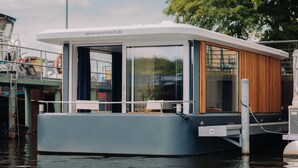 A modern houseboat with a covered deck, a wooden interior, and a number '70' sign. - Spreeapartment MARA (Berlin)