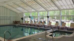 Una piscina interna con pareti di vetro trasparenti, poltrone relax e vista sull'esterno.