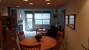 A dining area with a wooden table and chairs, a potted plant, and a view of the outdoors through large windows. - Gorgeous 3BR, 3BA Townhouse Right on the Pemi River - Great Views! (Lincoln)