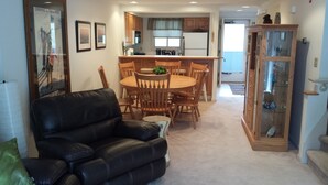 A dining area with a round table and chairs, a black leather sofa, and a cabinet with glass doors. - Gorgeous 3BR, 3BA Townhouse Right on the Pemi River - Great Views! (Lincoln)