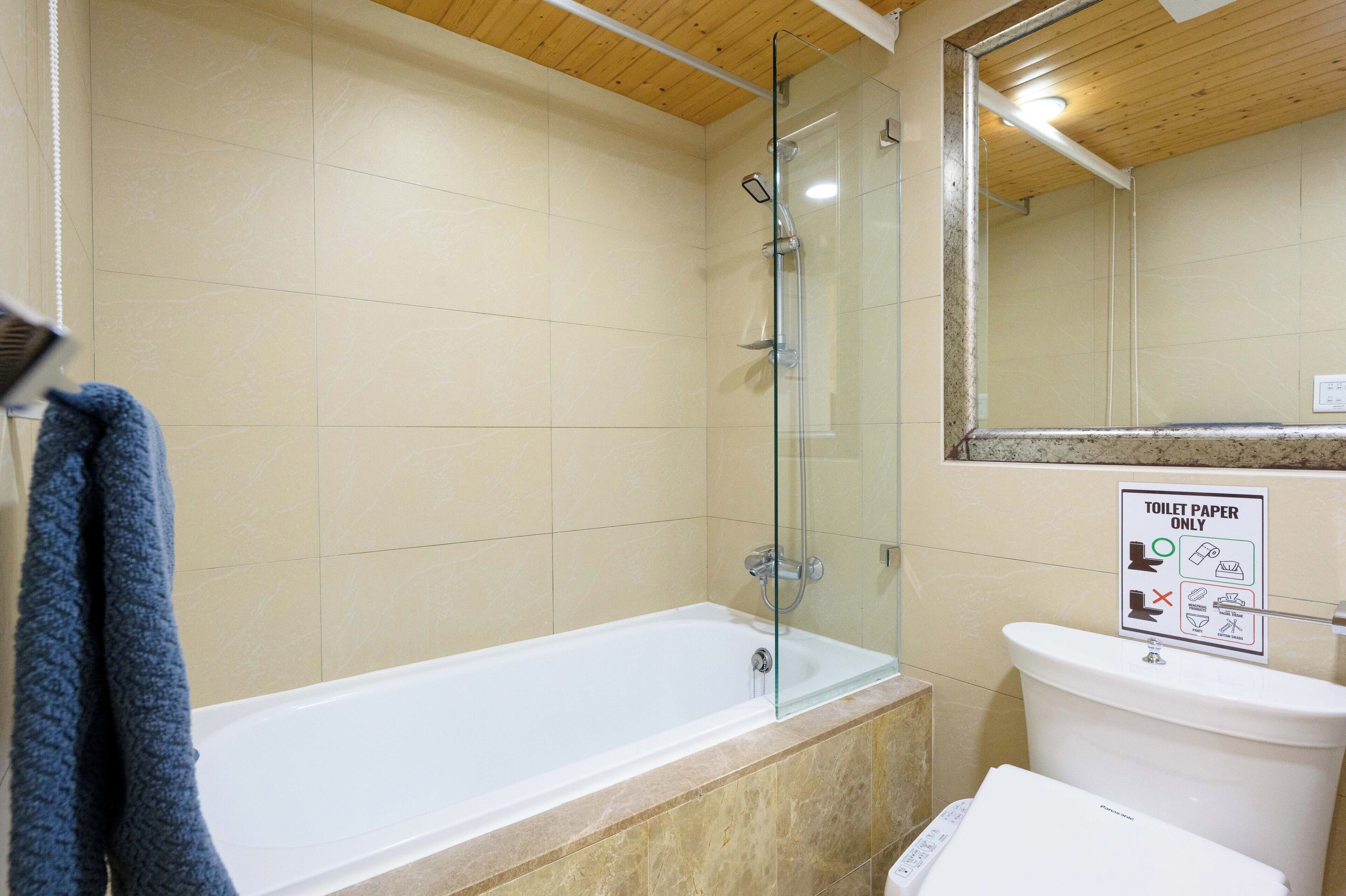 A bathroom with a glass-enclosed shower, a bathtub, and a toilet. There is a sign indicating the use of toilet paper only.