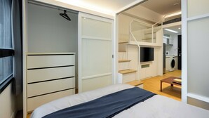 Quarto com cama, guarda-roupa, escrivaninha e escada que leva a um andar superior.