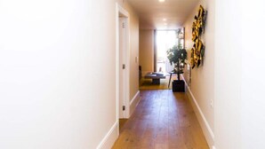 Un couloir avec un plancher en bois, des murs blancs et un banc au fond.