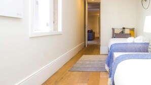 Un couloir étroit mène à une chambre à coucher qui contient un lit, une table de chevet et une fenêtre.