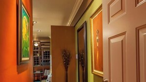 Un couloir avec une porte en bois, un vase et des œuvres d’art encadrées accrochées aux murs.
